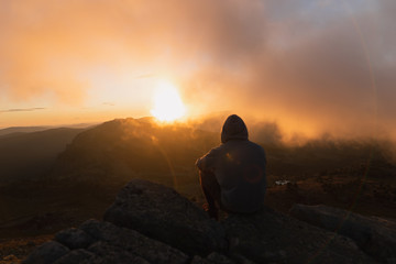 Man standing and watching a colorful sunrise in the mountains.