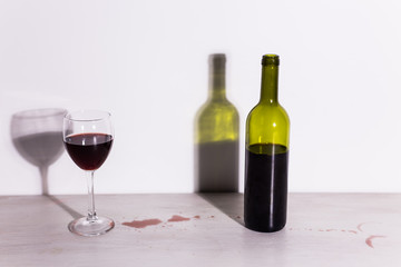 Bottle with wine and glass, red puddle of wine on the table. Cleaning after party concept.