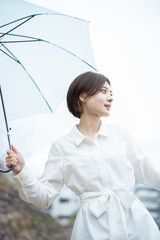 雨の中傘をさして歩く白いワンピースを着た若い女性