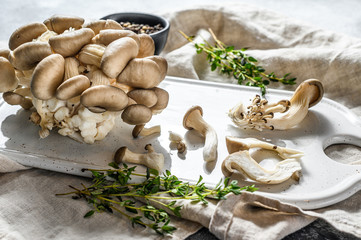 Raw oyster mushrooms on a white chopping Board with thyme. Gray background. Top view