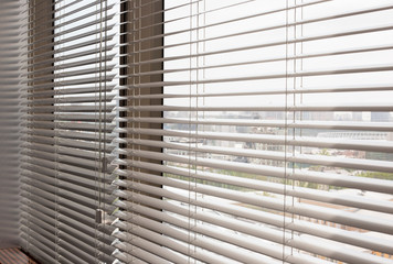 Aluminum blinds. Made from metal. Venetian blinds closeup on the window. Silver color. City landscape is in the background. Modern sun protection and window decoration.