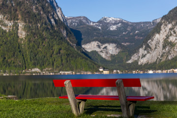red bench on the shore of a lake between mountains in Austria