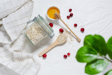 Fresh organic oat flakes with honey and cranberry on white concrete background top view. Healthy breakfast ingredients.
