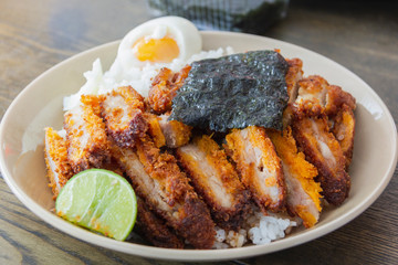 Pork fried rice with boiled eggs, sliced with lemon, sprinkled with seaweed sheets on a brown plate placed on a wooden table