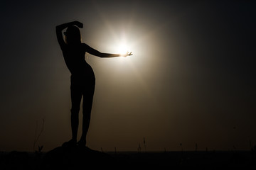 Silhouette of a girl at sunset standing on a rise. © gladiusstock