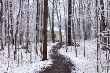 Path in wooded area covered in a light late spring fresh snow fall with a small yellow brick cottage in the background, Quebec City, Quebec, Canada