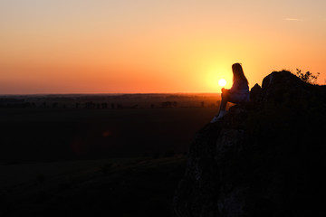 Silhouette of a woman sitting on a rock and watching in the distance.