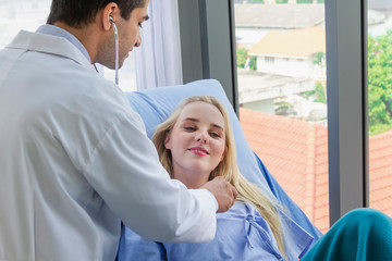 Caucasian female patient in bed and doctor use stethoscope analyze symptom sick at hospital