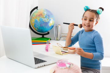 little girl learning make up powder, brush, blush on laptop online, distance learning