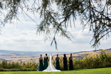 The bride and her girlfriends are holding hands. Looking at the mountains.