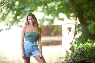 Stunning young Caucasian woman in green strapless top stands in shallow creek