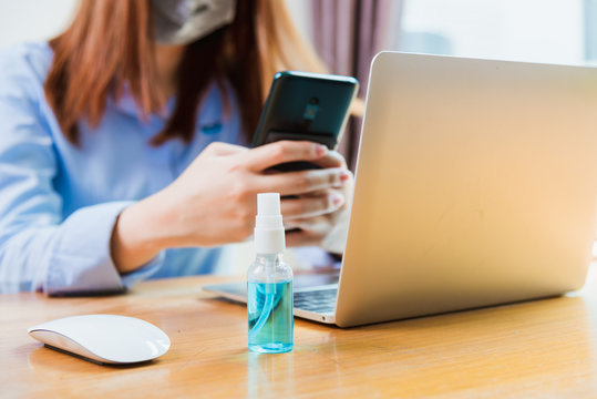 Asian young business woman wearing face mask protective using smart mobile phone for reading SMS message near laptop computer at home office quarantines disease coronavirus or COVID-19, work from home