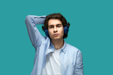 I don't care. Portrait of a young beautiful man wearing white t-shirt and blue shirt in headphones threw hand behind his head looking at camera