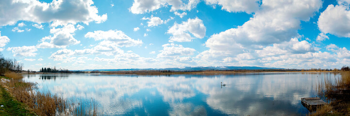 Panoramic landscape from the lake shore with colorful clouds in the spring sun.