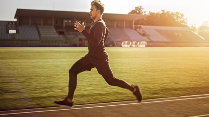 Athletic Fit Man in Grey Shirt and Shorts Jogging in the Stadium. He is Running Fast on a Warm...