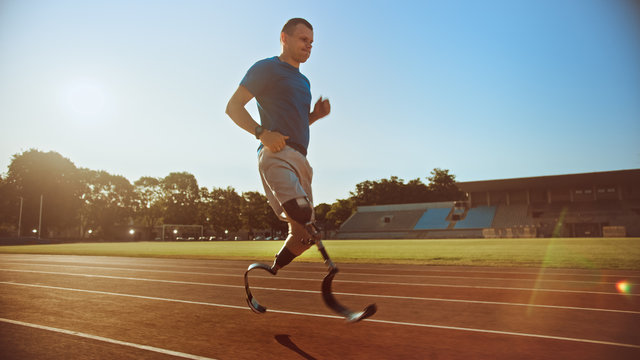 Athletic Disabled Fit Man with Prosthetic Running Blades is Training on an Outdoors Stadium on a Sunny Afternoon. Amputee Runner Jogging on a Stadium Track. Motivational Sports Shot.
