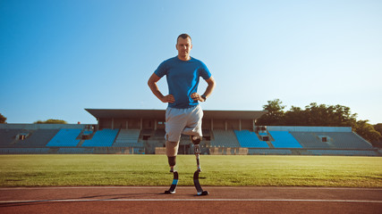 Athletic Disabled Fit Man with Prosthetic Running Blades is Posing During a Training on an Outdoor Stadium on a Sunny Afternoon. Amputee Runner Standing on a Track. Motivational Sports Shot.