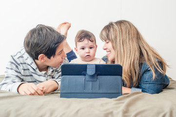 front view of a happy family using the tablet in bed.