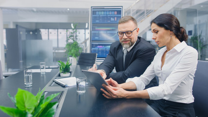 In the Meeting Room Female Executive Shows Digital Tablet Computer to Male Investor, They Discuss Statistics and Venture Investing Potential. Busy Corporate Office with Businesspeople Working