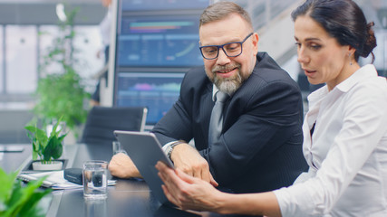 In the Meeting Room Female Executive Shows Digital Tablet Computer to Male Investor, They Discuss Statistics and Venture Investing Potential. Busy Corporate Office with Businesspeople Working