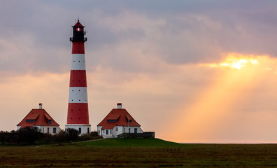 The sun shines through a hole in the clouds almost directly onto the lighthouse.