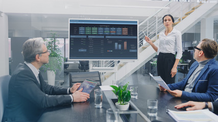 In the Corporate Meeting Room: Female Analyst Uses Digital Interactive Whiteboard for Presentation to a Board of Executives, Lawyers, Investors. Screen Shows Company Growth Data with Animated Graphs