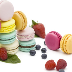 Multicolored macaroons on a white background with strawberries, raspberries, mint and blueberries