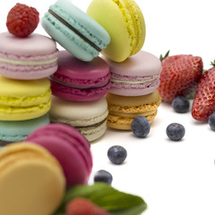 Multicolored macaroons on a white background with strawberries, raspberries, mint and blueberries