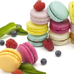 Multicolored macaroons on a white background with strawberries, raspberries, mint and blueberries
