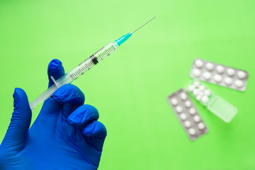 Hand in blue gloves holding a syringe and pills on a light green background. Concept of coronavirus...