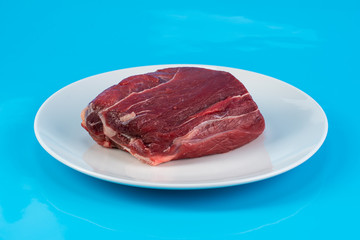 piece of raw beef meat tenderloin on a white plate on a blue background