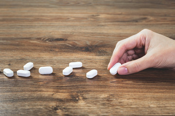 Hand with white tablets pills lined on wooden table. Pharmacy. Healthcare and medicine concept drugs safety consumption or misuse with copy space. Medication