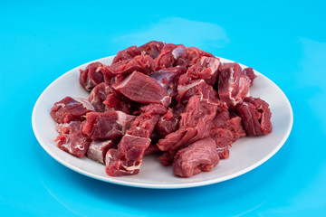 chopped small pieces of raw beef meat, tenderloin on a white plate on a blue background