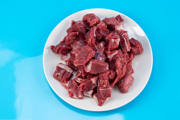 chopped small pieces of raw beef meat, tenderloin on a white plate on a blue background
