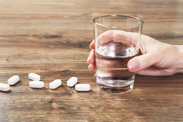 Hand with white tablets or pills lined on wooden table with glass of water. Pharmacy. Healthcare...