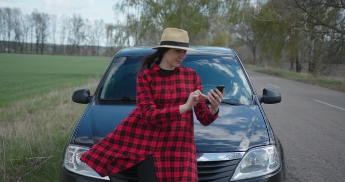 Hipster tourist woman in red dress near car on the road route planning in navigation maps app on smartphone.
