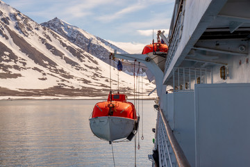 Lowering orange lifeboat to water in Arctic waters, Svalbard. Abandon ship drill. Lifeboat...