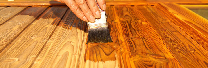 Lasurer. Painting woodwork outside. hand of Handyman varnishing a wooden door. Concept of...