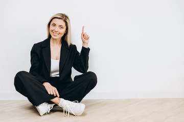 A beautiful young woman is sitting on the floor against a light background, with copy space left