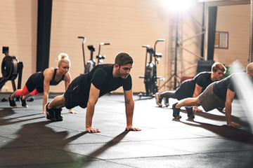 Group of fit people doing pushups together at the gym