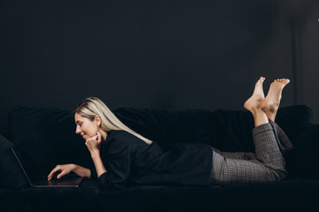 A pretty young woman on the black sofa is a using a notebook, background is black