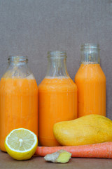 Glass bottles filled with colorful fresh homemade mango, carrot and ginger smoothies