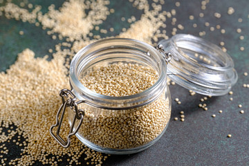 White raw quinoa in glass jar on green rustic background. Healthy and gluten free food. Copy space.