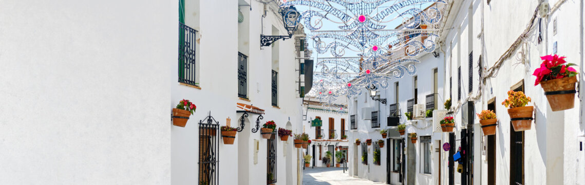 Fototapeta Panoramic image white copy space view, empty street famous village of Mijas in Spain. Charming narrow streets with New Year decorations, hanging flower pots on walls, no people. Costa del Sol, Malaga