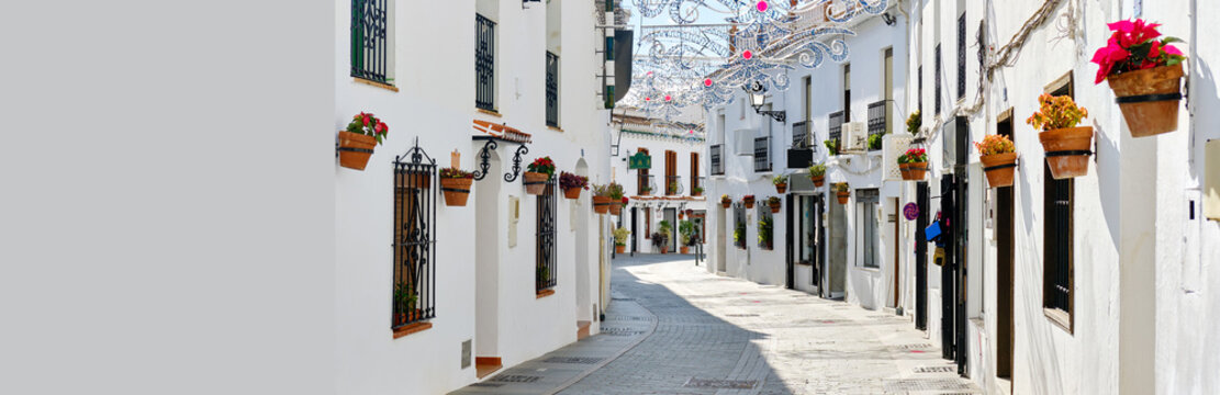 Fototapeta Panoramic image white copy space view, empty street famous village of Mijas in Spain. Charming narrow streets with New Year decorations, hanging flower pots on walls, no people. Costa del Sol, Malaga