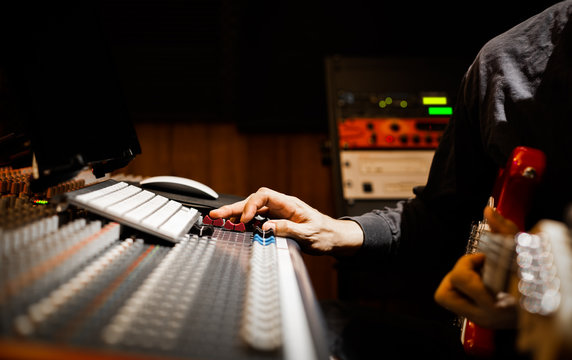 male musician recording electric guitar on audio mixing board and computer in home recording studio