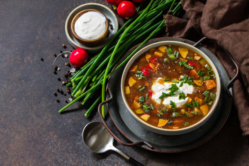 Traditional dish Russian cuisine. Cold summer Okroshka soup with kvass, sausage and vegetables in a bowl on a dark stone countertop. Copy space.