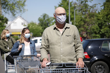 Älterer Mann mit Mundschutz steht mit einem Einkaufswagen geduldig in einer Warteschlange