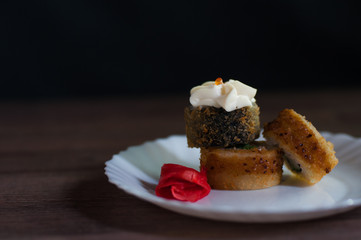 Fried sushi on a white plate with greens, cream cheese and ginger on dark background front view