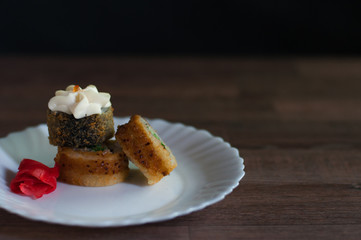 Fried sushi on a white plate with greens, cream cheese and ginger on dark background front view